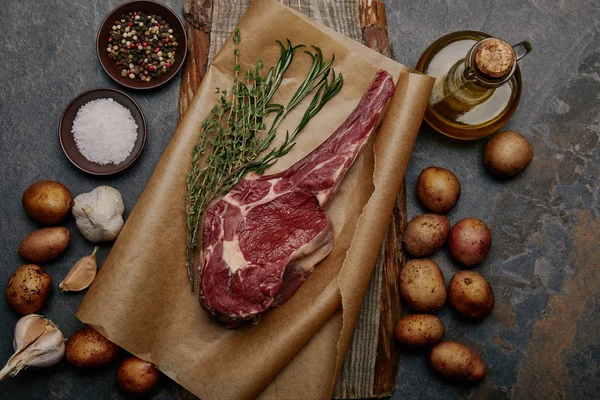 Roh Rib Eye Steak auf Backpapier mit Gewürzen, Kräutern und Kartoffeln auf grauem Hintergrund — Stockfoto