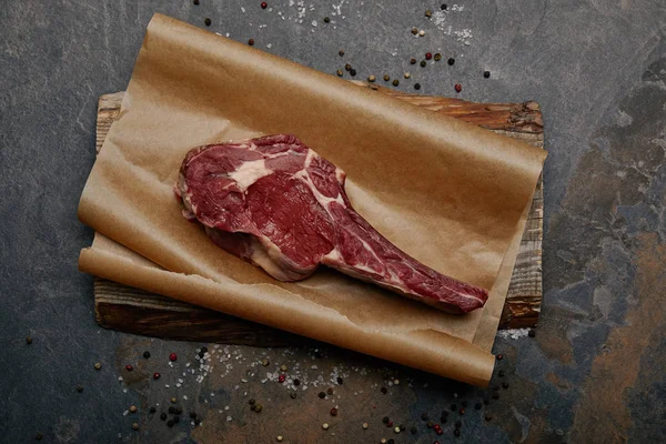 Top view of raw rib eye steak on baking paper with spices on grey background — Stock Photo