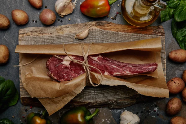 Filete de costilla crudo envuelto en papel de hornear sobre tabla de madera con hierbas, especias y papas - foto de stock