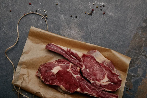 Vue du dessus des biftecks crus sur papier cuisson avec épices sur fond gris — Photo de stock