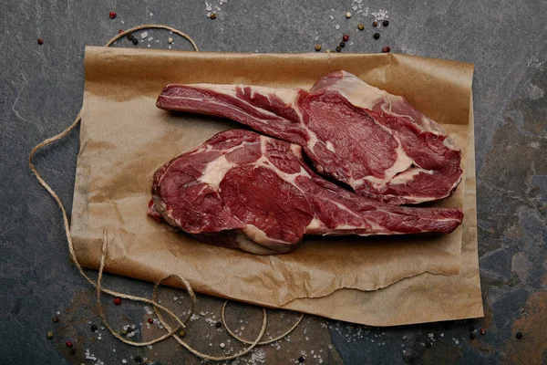 Vue du dessus des biftecks crus sur papier cuisson avec épices sur fond gris — Photo de stock