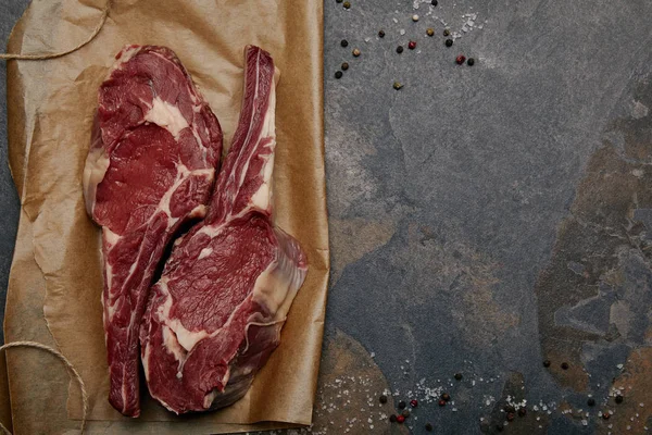 Top view of raw rib eye steaks on baking paper with spices on grey background — Stock Photo