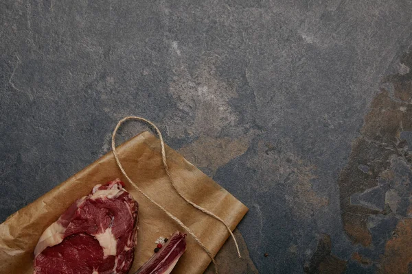 Vista dall'alto della bistecca di carne cruda su carta da forno su fondo grigio — Foto stock