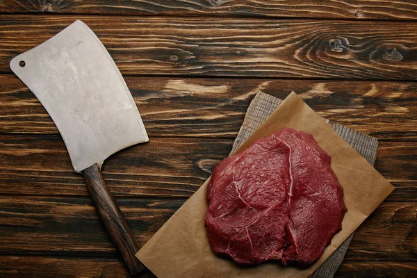 Vue de dessus de la viande crue sur papier cuisson avec couteau de boucher sur fond en bois — Photo de stock