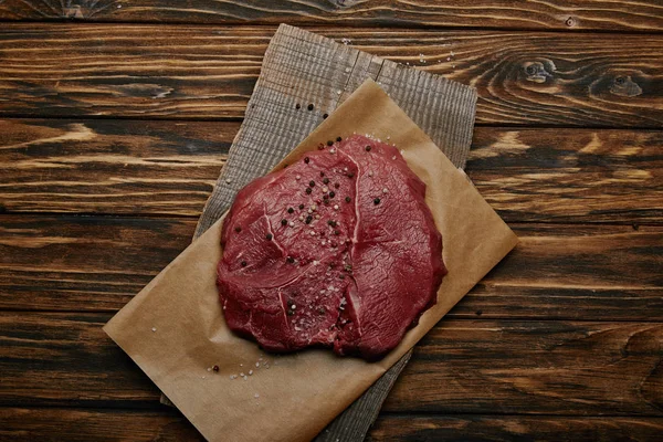 Вид зверху сирого свіжого м'яса на папері для випічки на дерев'яному фоні — стокове фото