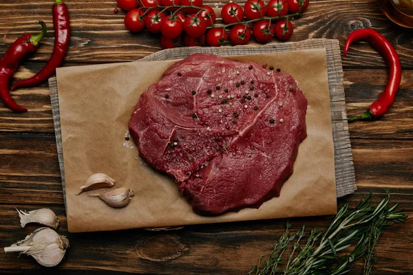 Flat lay with fresh raw meat on baking paper with garlic and vegetables on wooden background — Stock Photo