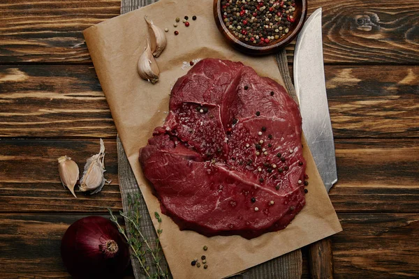 Poser à plat avec de la viande fraîche crue sur du papier cuisson avec de l'ail et des épices sur fond en bois — Photo de stock