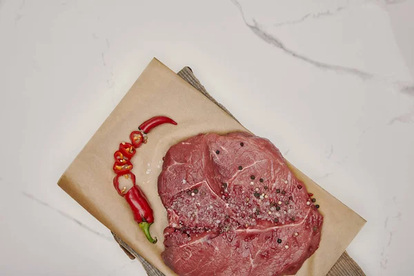 Ansicht von frischem rohem Fleisch auf Backpapier mit gehackter Chilischote auf weißem Hintergrund — Stockfoto