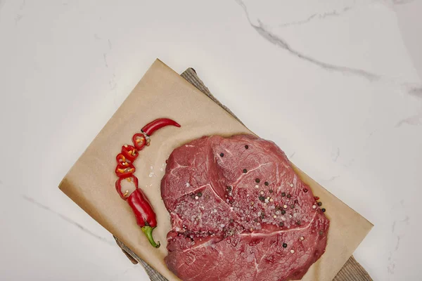 Top view of fresh raw meat on baking paper with chopped chilli pepper on white background — Stock Photo