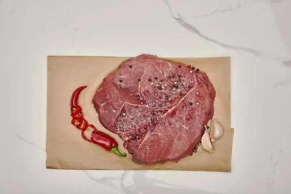 Ansicht von frischem rohem Fleisch auf Backpapier mit gehackter Chilischote und Knoblauch auf weißem Hintergrund — Stockfoto