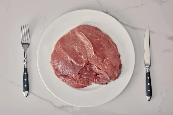 Ansicht von frischem rohem Fleisch auf Teller mit Küchenbesteck auf weißem Hintergrund — Stockfoto