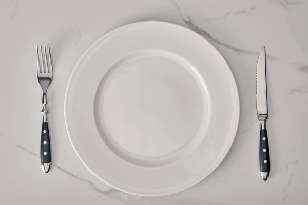 Plaque vide avec fourchette et couteau sur fond de marbre blanc — Photo de stock