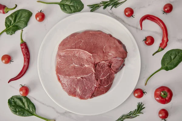 Плоская выложи свежее сырое мясо на тарелку с овощами и зеленью на белом фоне — стоковое фото