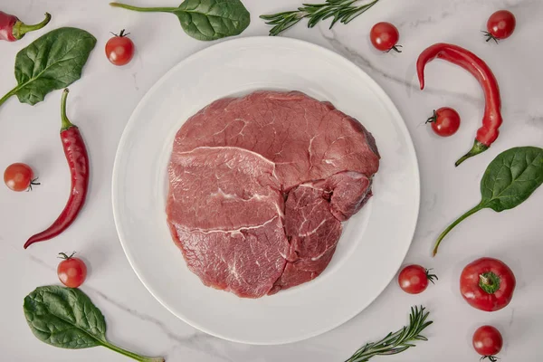 Acostado plano con carne fresca cruda en el plato con verduras y hierbas sobre fondo blanco - foto de stock