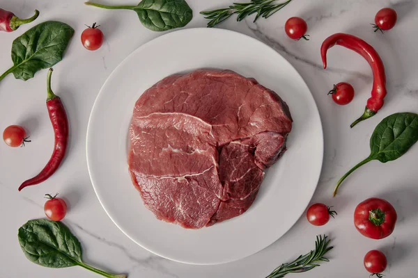 Vista dall'alto di carne fresca cruda su piatto con verdure ed erbe su sfondo bianco — Foto stock