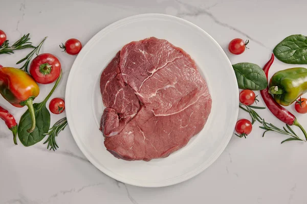 Vue du dessus de viande fraîche crue sur assiette avec des légumes et des herbes sur fond blanc — Photo de stock