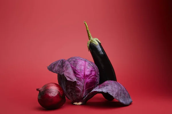 Cebolla orgánica fresca madura, col y berenjena sobre fondo rojo - foto de stock