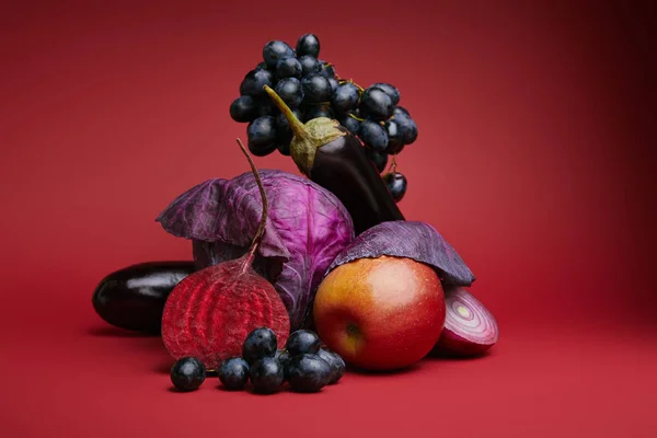 Vista de cerca de uvas frescas maduras, manzana, col, remolacha, cebolla y berenjenas sobre fondo rojo - foto de stock