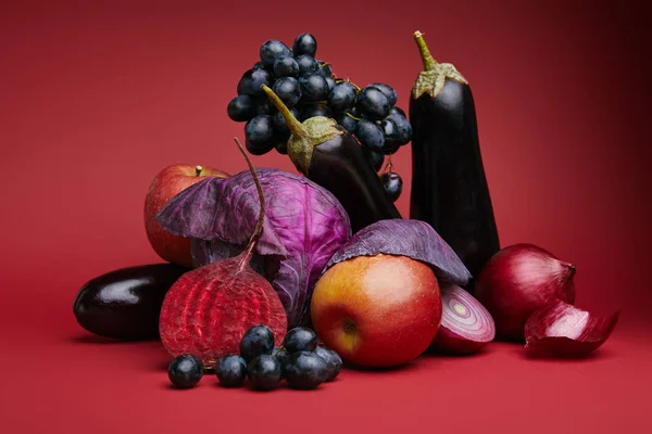 Vista de cerca de uvas frescas maduras, manzanas, berenjenas, remolacha, cebollas y repollo sobre rojo - foto de stock