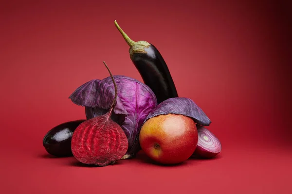 Крупный план зрелых органических яблок, капусты, баклажанов, лука и свеклы на красном фоне — стоковое фото