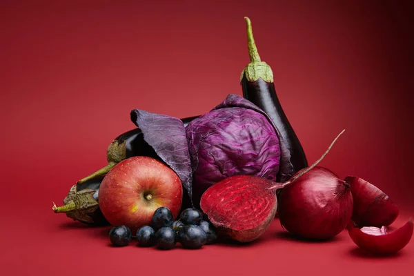 Close-up view of ripe organic apple, grapes, onions, beetroot, cabbage and eggplants on red — Stock Photo