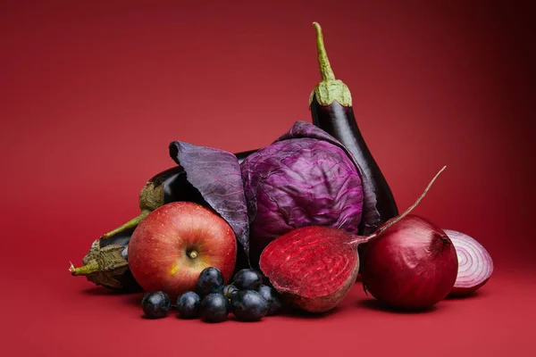 Manzana orgánica fresca madura, uvas, cebollas, remolacha, col y berenjenas sobre rojo - foto de stock