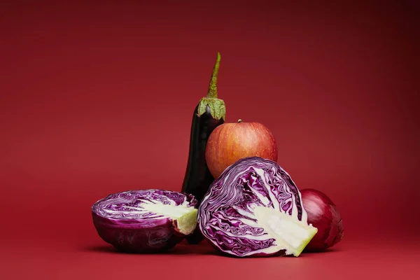 Fresh ripe apple, eggplant, onion and sliced cabbage on red background — Stock Photo