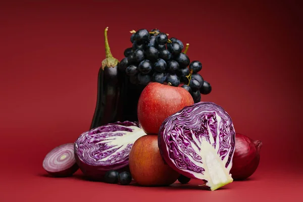 Vue rapprochée des pommes, raisins, aubergines, choux et oignons sur rouge — Photo de stock