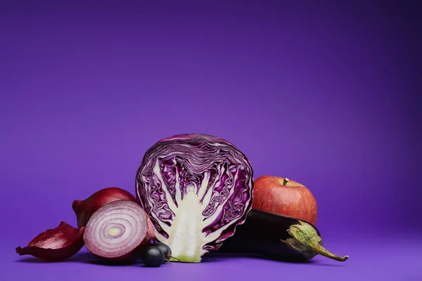 Vista de cerca de repollo en rodajas, cebollas, uvas, berenjena y manzana en púrpura - foto de stock
