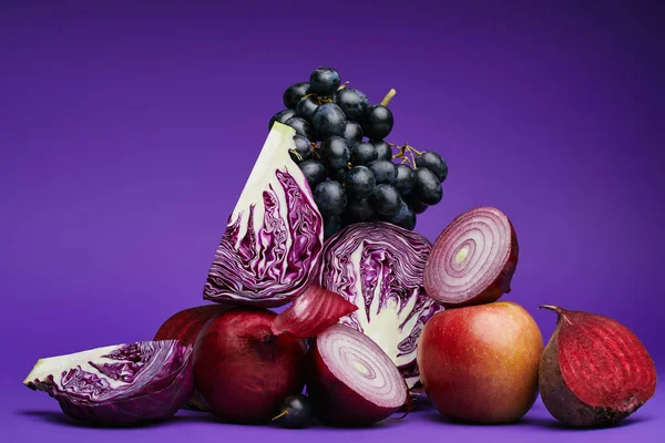 Vista de cerca de las uvas, manzana, remolacha, cebollas y repollo en rodajas en púrpura - foto de stock