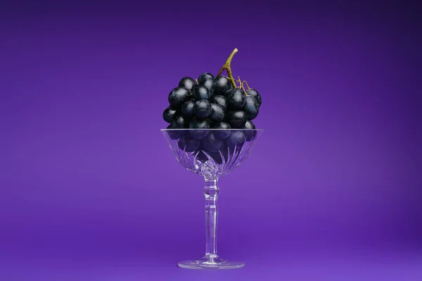 Vista de cerca de uvas frescas maduras en vidrio sobre fondo violeta - foto de stock