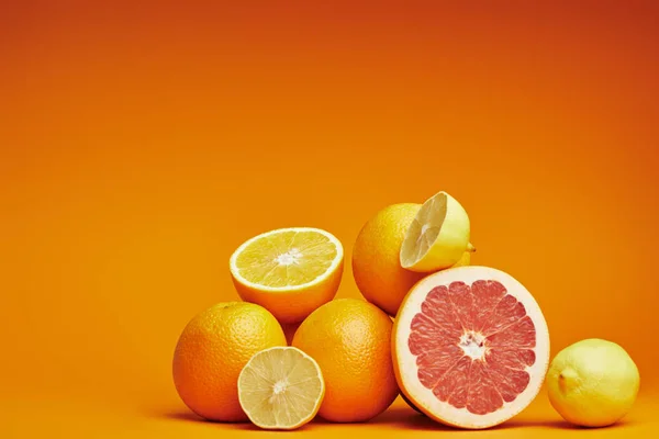 Cítricos frescos maduros enteros y cortados en rodajas sobre fondo naranja - foto de stock