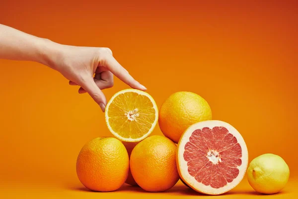 Cropped shot of human hand and fresh ripe citrus fruits on orange — Stock Photo