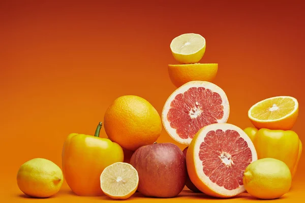 Fresh ripe organic citrus fruits, apples and bell peppers on orange background — Stock Photo