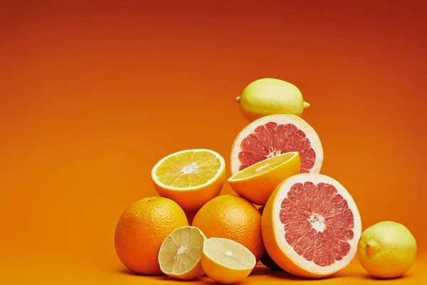 Vista de cerca de cítricos frescos maduros enteros y cortados en rodajas sobre fondo naranja - foto de stock