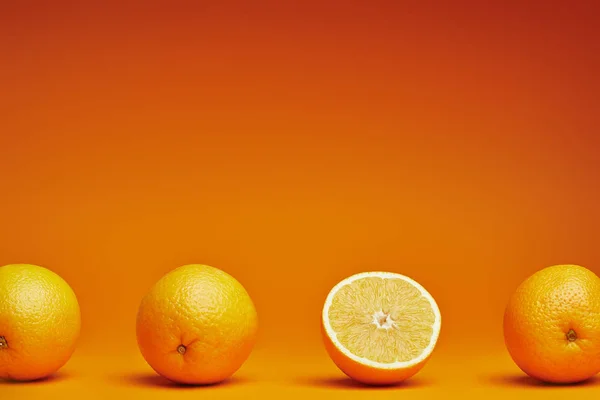 Vista close-up de laranjas maduras frescas inteiras e cortadas pela metade no fundo laranja — Fotografia de Stock