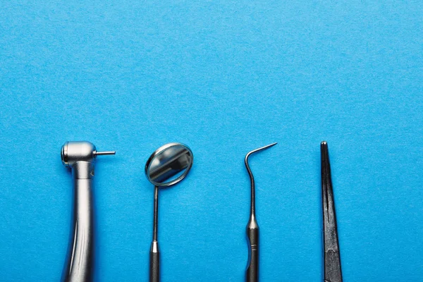 Leigos planos com instrumentos dentários inoxidáveis dispostos em mesa azul, odontologia e conceito de cuidados dentários — Fotografia de Stock