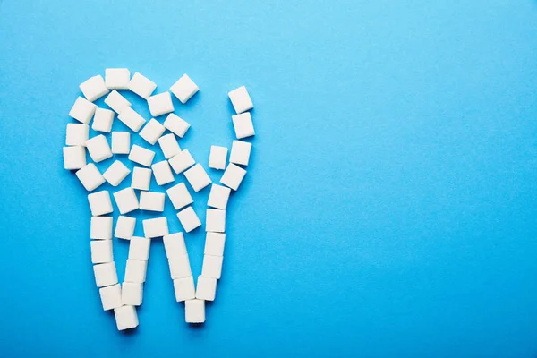 Vista superior de cubos de açúcar branco dispostos em sinal de dente no fundo azul, conceito de cuidados dentários — Fotografia de Stock