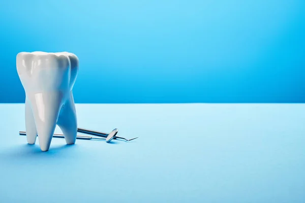 Vue rapprochée du miroir dentaire stérile, de la sonde et du modèle dentaire disposés sur fond bleu — Photo de stock