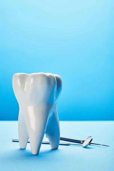 Vista de perto do espelho dental estéril, sonda e modelo de dente dispostos em fundo azul — Fotografia de Stock
