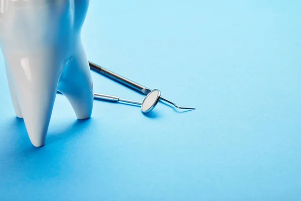 Vista de perto do espelho dental estéril, sonda e modelo de dente dispostos em fundo azul — Fotografia de Stock