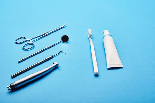 Vue rapprochée de la disposition des instruments dentaires stériles, stéthoscope, brosse à dents et dentifrice sur fond bleu, concept de soins dentaires — Photo de stock