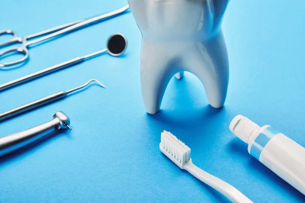 Vista de cerca del modelo de diente blanco, cepillo de dientes, pasta de dientes e instrumentos dentales inoxidables sobre fondo azul - foto de stock