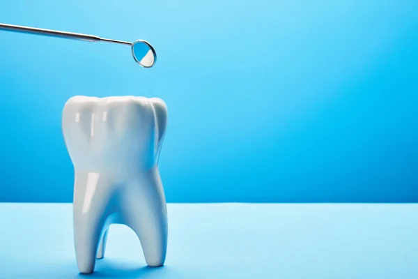 Close up view of tooth model and dental mouth mirror on blue backdrop — Stock Photo