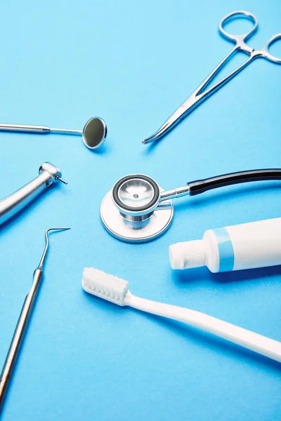 Close up view of arrangement of sterile dental instruments, stethoscope, toothbrush and toothpaste on blue backdrop, dental care concept — Stock Photo