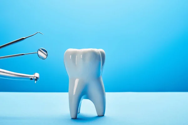 Vista de perto do modelo de dente branco e instrumentos dentários inoxidáveis no fundo azul — Fotografia de Stock