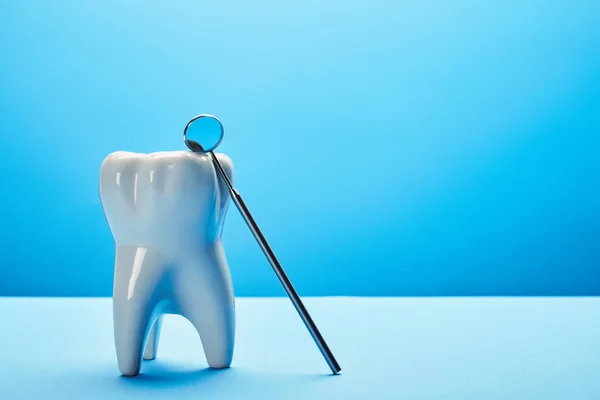 Close up view of tooth model and dental mouth mirror on blue backdrop — Stock Photo