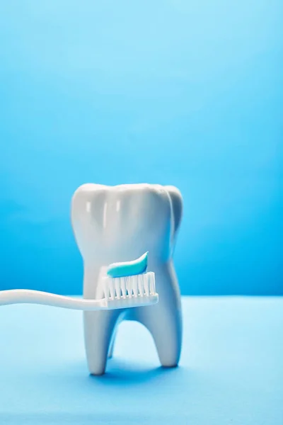 Primo piano vista del modello di dente e spazzolino da denti con pasta su sfondo blu, concetto di cura dentale — Foto stock
