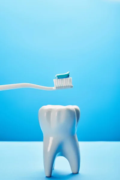 Vista de perto do modelo de dente e escova de dentes com pasta em fundo azul, conceito de cuidados dentários — Fotografia de Stock