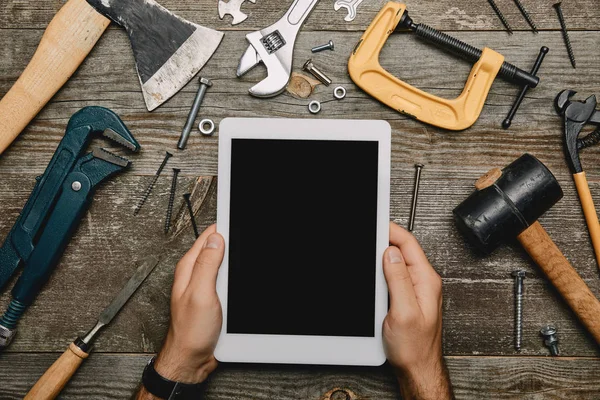 Teilansicht des Menschen mit digitalem Tisch mit leerem Bildschirm auf hölzernem Hintergrund mit verschiedenen Werkzeugen — Stockfoto